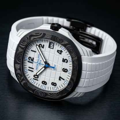 White carbon grid-dial watch at a three-quarter angle on dark slate, grey-black layer lines along the white case flank and a black fluted crown