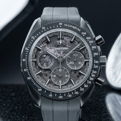 Grey ceramic chronograph on a grey ribbed rubber strap, worn on a wrist below a navy suit cuff