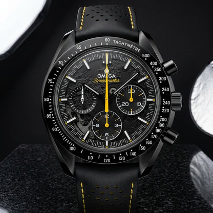 Black ceramic moon chronograph on a black perforated strap with yellow stitching, worn on a wrist below a navy suit cuff