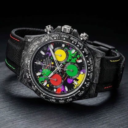 Forged-carbon chronograph with a paint-splash dial at a three-quarter angle on dark slate