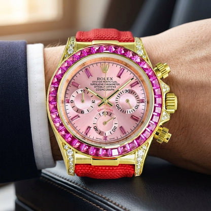 Gold-tone chronograph with a pink dial and a pink stone bezel on a red canvas strap, worn on the wrist below a navy suit cuff