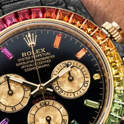 Macro of the glossy black dial with coloured stone hour markers and three champagne-gold counters inside the gold-set rainbow bezel
