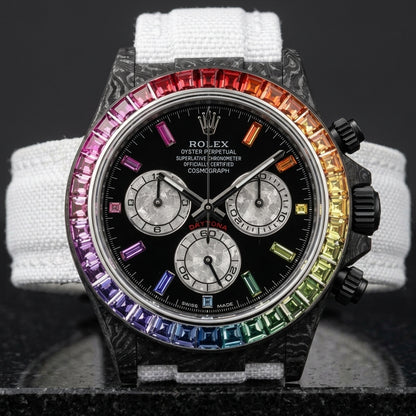 Black carbon chronograph with a rainbow bezel on its white woven strap, worn on the wrist below a navy suit cuff