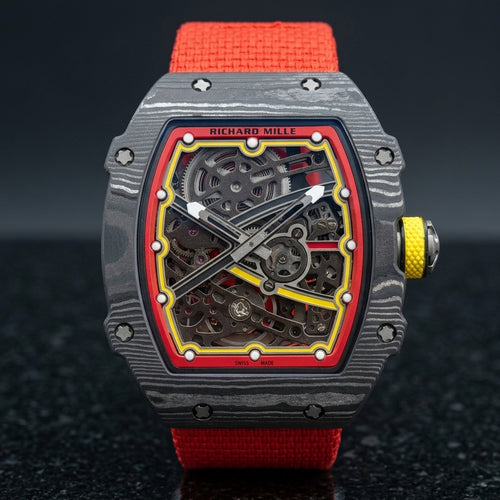 Carbon tonneau skeleton watch with a red flange and yellow track on a red elastic strap, upright on polished black granite