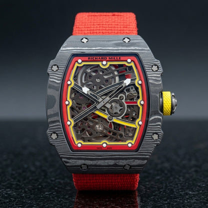 Carbon tonneau skeleton watch on its red elastic strap, worn on the wrist below a dark suit cuff