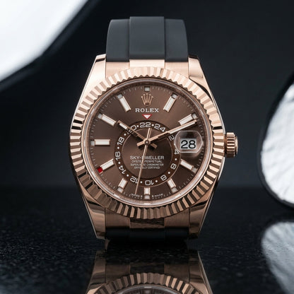 Rose-gold dual-time watch with a chocolate sunray dial and fluted bezel, upright on polished black granite