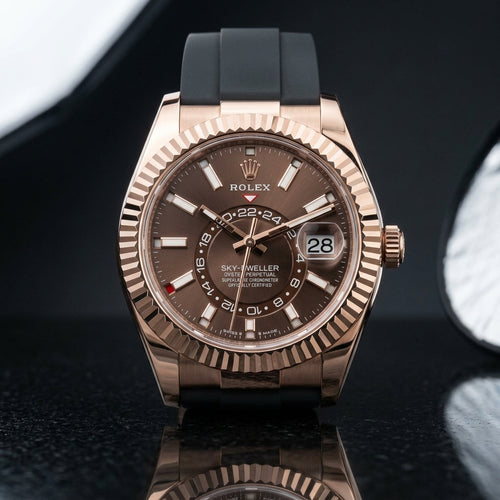 Rose-gold dual-time watch with a chocolate sunray dial and fluted bezel, upright on polished black granite