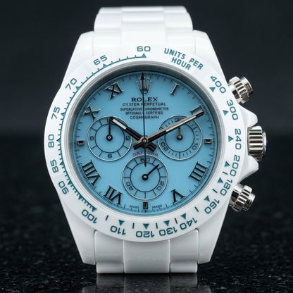 White ceramic chronograph with a light blue dial on its white ceramic bracelet, worn on the wrist below a dark suit cuff