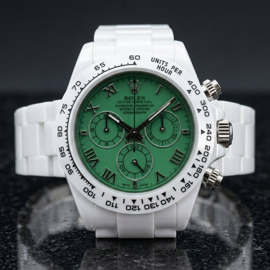 White ceramic chronograph with a green Roman numeral dial and a white tachymeter bezel, upright on polished black granite