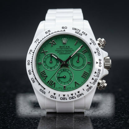 White ceramic chronograph with a green dial on its white ceramic bracelet, worn on the wrist below a dark suit cuff
