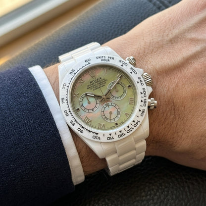 White ceramic chronograph with a green mother-of-pearl dial on the wrist below a dark suit cuff