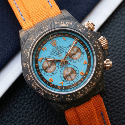 Forged-carbon chronograph on an orange woven strap, worn under a cuff