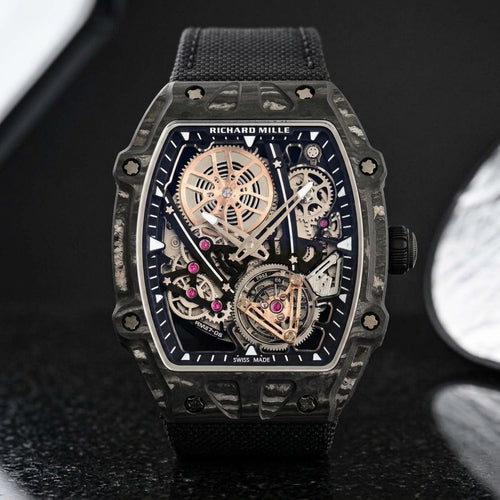 All-black thin-ply carbon tonneau watch with an open skeleton dial and a black woven strap, upright on polished black granite