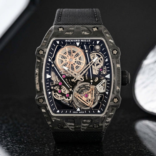 All-black thin-ply carbon tonneau watch with an open skeleton dial and a black woven strap, upright on polished black granite