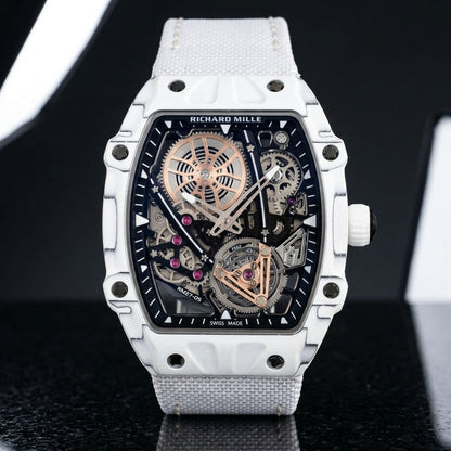 All-white thin-ply carbon tonneau watch with an open skeleton dial and a white woven strap, upright on polished black granite