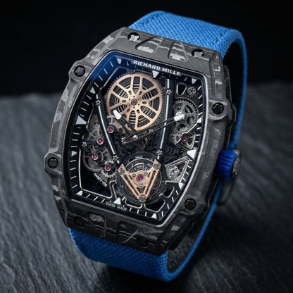 Black carbon skeleton watch at a three-quarter angle on dark slate, grey-silver grain across the bezel and a ribbed blue crown