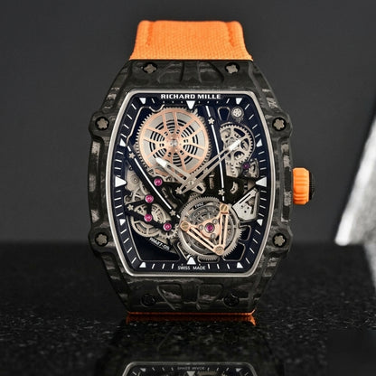 Black carbon skeleton tourbillon watch on an orange woven strap, worn on the wrist below a navy suit cuff