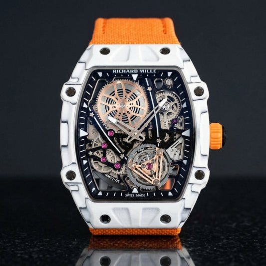 White thin-ply carbon tonneau watch with an open skeleton dial and an orange woven strap, upright on polished black granite