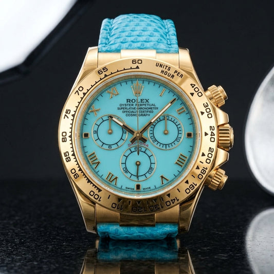 Gold-tone chronograph with a turquoise dial, gold Roman numerals and an engraved tachymeter bezel standing upright on polished black granite
