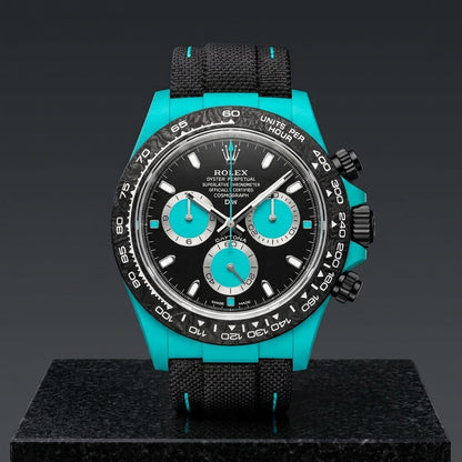 Turquoise-cased chronograph on a black woven strap with turquoise stitching, worn under a cuff