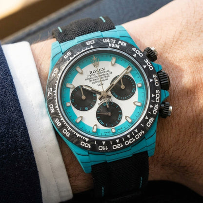 Turquoise-cased chronograph on a black woven strap with turquoise stitching, worn under a cuff