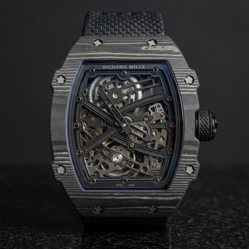 All-black carbon tonneau skeleton watch with a black X over the open movement, upright on polished black granite
