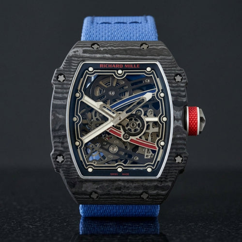 Ultra-thin black carbon tonneau watch with a blue and red skeleton dial and a blue textile strap, upright on polished black granite