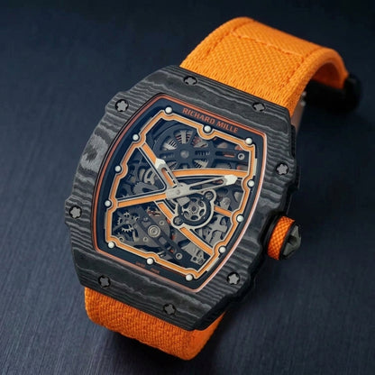 Black carbon tonneau watch at a three-quarter angle on dark slate, grey layer waves across the case and an orange honeycomb-grip crown