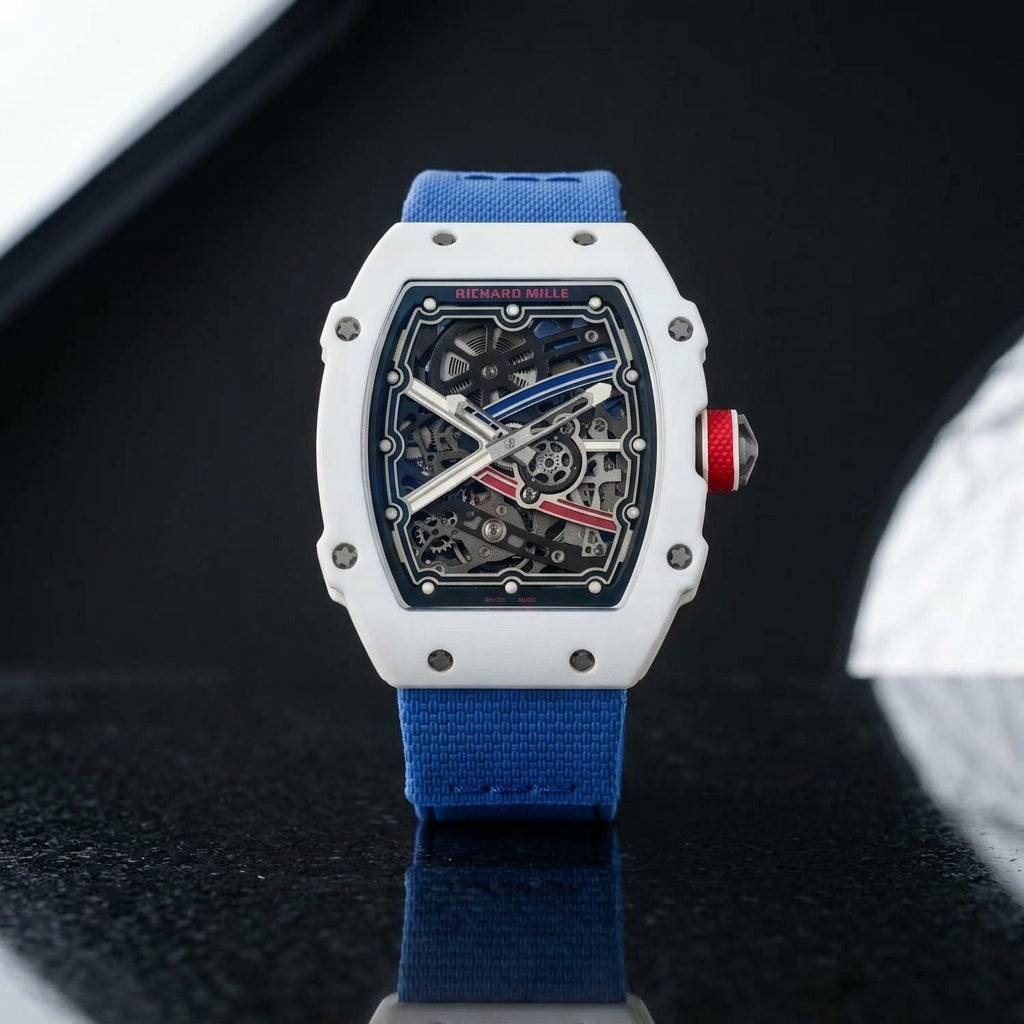 White tonneau watch with a red crown on a blue textile strap, worn on the wrist below a navy suit cuff