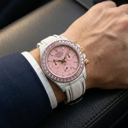 White carbon chronograph with a pale pink stone bezel on its white woven strap, worn on the wrist below a cream sleeve