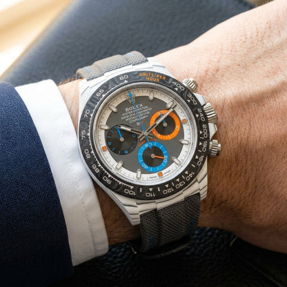 White CarboQuartz chronograph on a grey woven strap with blue stitching, worn under a cuff